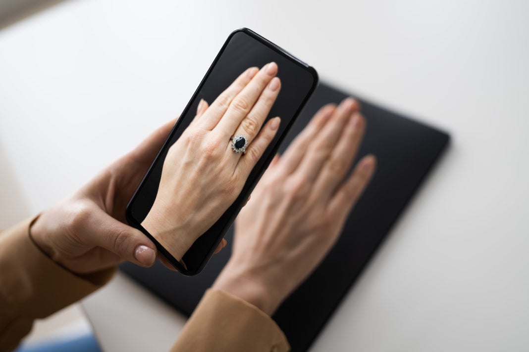 Image of person holding smartphone camera over their hand to simulate a virtual try-on experience using augmented reality.