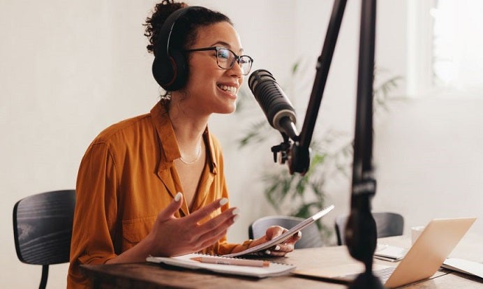 woman podcaster sitting at desk speaking into microphone